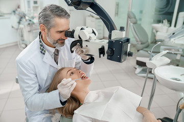 Doctor looking through dental microscope at teeth of woman.