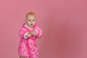 Little girl in a pink bathrobe on a pink background in the studio.