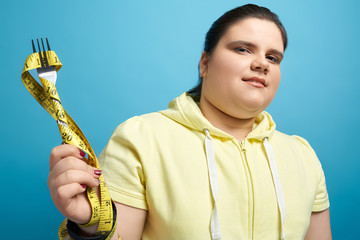 Pretty fat lady keeping fork wrapped by measuring tape
