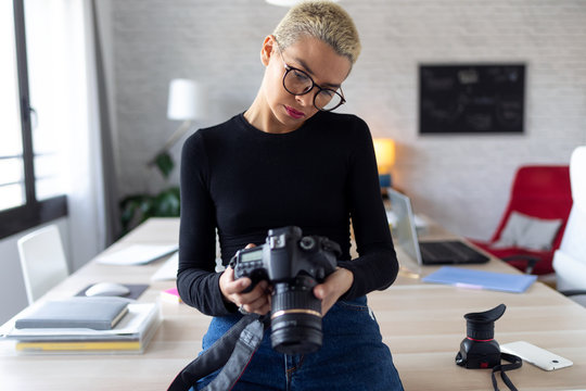 Modern young entrepreneur woman reviewing her last photographs in the camera while sitting in the office.