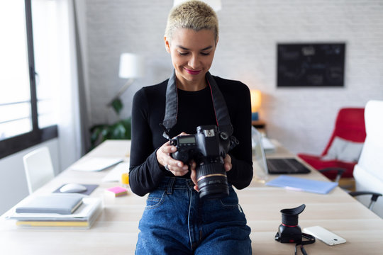 Smiling young entrepreneur woman reviewing her last photographs in the camera while sitting in the office. - Powered by Adobe