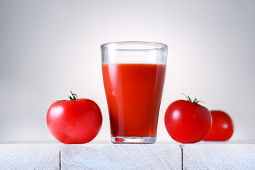Glass of fresh organic tomato juice with raw tomatoes on light wooden table.