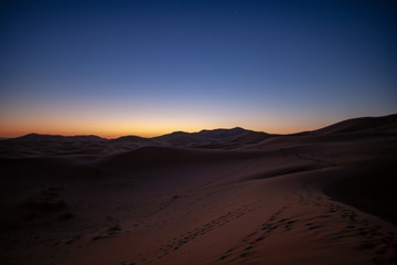 Fototapeta na wymiar Erg Chebbi, Morocco, sand dunes of Sahara desert formed by wind are awakening in the first rays of the day, illuminated by the sun.