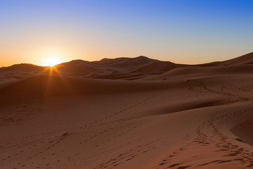 Obraz na płótnie Canvas Erg Chebbi, Morocco, sand dunes of Sahara desert formed by wind are awakening in the first rays of the day, illuminated by the sun.