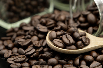 Roasted coffee beans in wooden spoon and spread on black table with bottle glass