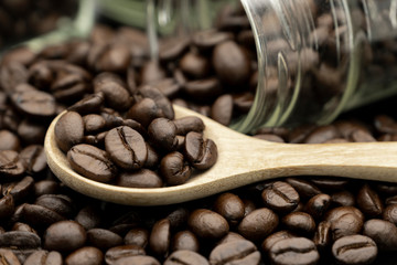 Roasted coffee beans in wooden spoon and spread on black table with bottle glass