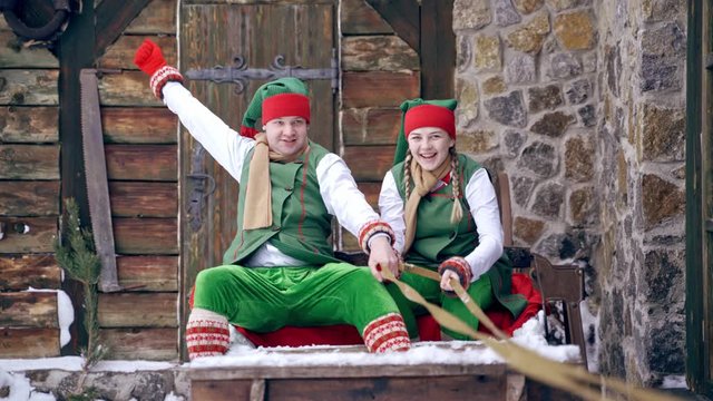 Christmas elves ride wooden sledges. New Year is coming. Christmas eve. Boy and girl wear christmas clothes. Having fun.