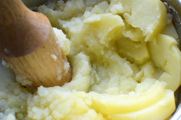 Mashed potatoes cooking, making process with a wooden mesher in a sucepan
