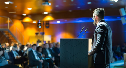 Speaker giving a talk on corporate business conference. Unrecognizable people in audience at...