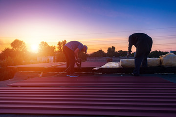 A man holds a board on the roof. Men mount the roof on the building. People are blurred. Focus at...