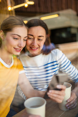 Close up happy mother and daughter sitting at cafe looking at cellphone