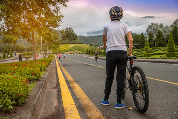 Naklejka premium Woman standing with bike looking at on sunset, Bike at the summer sunset on road in the park.