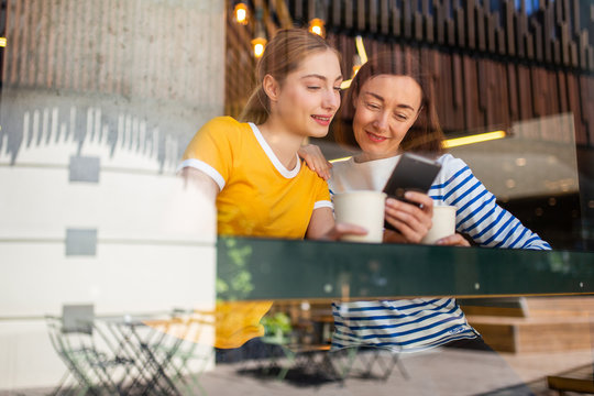 mother and daughter at cafe looking at cellphone together