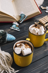 Mugs with marshmallows near Christmas toys and book