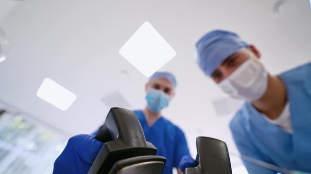 Defibrolator in hands from the eyes of a patient. Blue medical clothes. First aid. External Pacer Analyzer,Using a defibrillator to save lives.