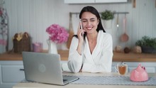 Beautiful woman talking on phone, sitting on kitchen in morning time