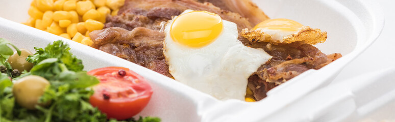 panoramic shot of eco package with corn, meat, fried egg and salad on white background