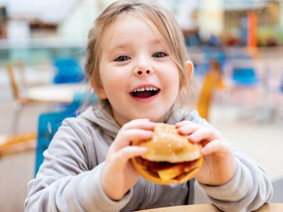 Cute little girl eating fast food hamburger in cafe