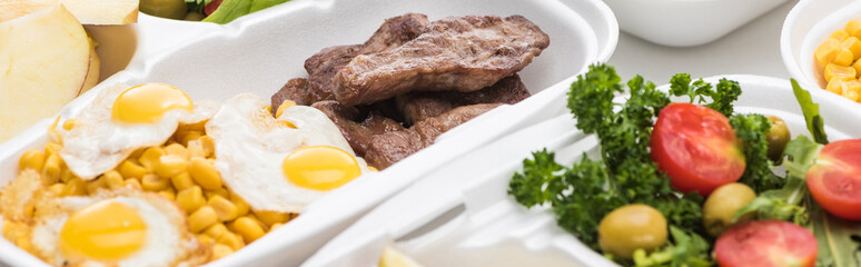 panoramic shot of eco package with corn, meat, fried eggs and salad on white background