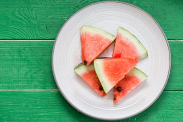 Sliced watermelon on a plate and uncut watermelon on a green wooden table. Top view