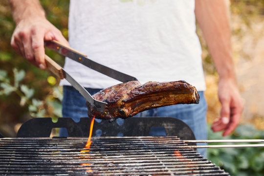 cropped view of man with tweezers grilling meat on barbecue grid