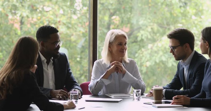 Smiling mature female leader discuss project with team at meeting