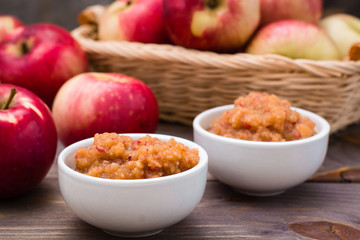Fresh applesauce in bowls and red apples on a wooden table