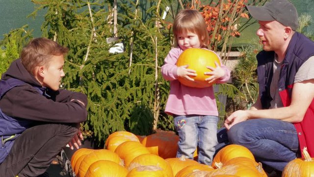 Father and kids selecting pumpkin, having fun in garden. Family choosing vegetable for Halloween or Thanksgiving day from pumpkin patch. Dad and kids choosing orange pumpkin, daughter hugging squash