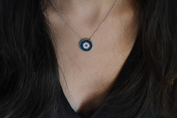 Dark haired women wearing a evil or blue eye silver necklace around her neck demonstrating her...