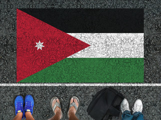 people legs are standing on asphalt road next to flag of  Jordan and border