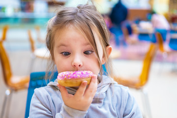 Cute girl eating a donut in a cafe. Funny portrait of a child