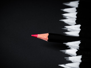 Black and white picture of the pencils with one red coloured pecncil in the middle on a black...