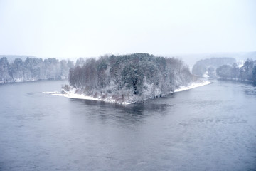 Snow-covered island of winter forest among river