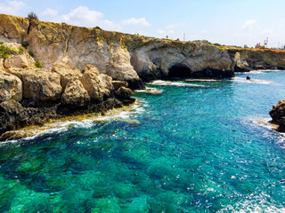 Fototapeta premium Turquoise sea water with grey natural stones. Purity ripple ocean water surface with selective focus and sun light. Transparent blue water surface with rocks.