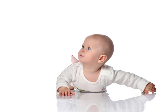 Curious infant baby toddler in white bodysuit is lying on his stomach looking up at free copy space near him on white