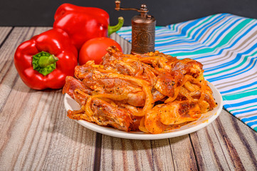 Lamb ribs marinated with spices in a plate on the table. With tomatoes and sweet peppers.