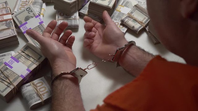 Jail prisoner at a table in handcuffs with a lot of cash money around him.