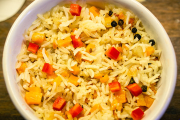 Yellow rice with slices of red bell pepper and dark pepper. In a white bowl. on a wooden surface. warm tone. Horizontal orientation.