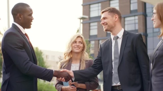Medium shot of optimistic business people discussing work outdoors, two men shaking hands and smiling