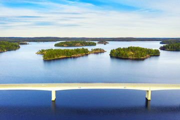 Aerial view of modern bridge with cars across blue lake Saimaa at summer sunset time. Beautiful sky with clouds. Finland