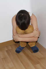 offended boy sitting in the corner, hiding his face in his knees, educational concept