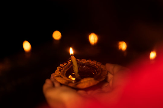 Person Hand Holding Diya on Diwali. Indian woman or female holding diya or oil lamp in her hand during diwali celebration night. Background image for stock photo of Diwali.