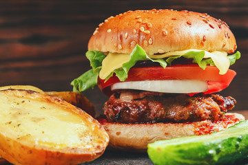 Fresh homemade burger and baked potatoes with cucumber on a slate dish on a wooden background