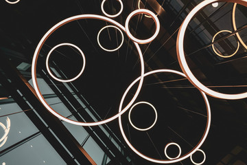 Light ring fixtures hanging from the building ceiling, dark architectural concept photo