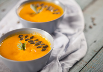 Delicious creamy pumpkin and carrot soup with seeds, bread and parsley close-up on a blue background.