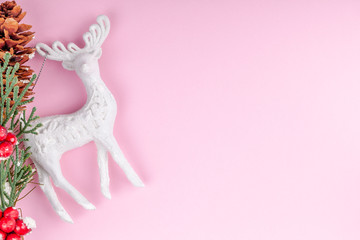 White Christmas deer toy with New Year holidays pine tree and cone decoration on pink paper background. Copy space. Xmas greeting card concept.