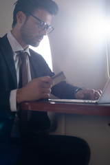handsome businessman with credit card and laptop in airplane