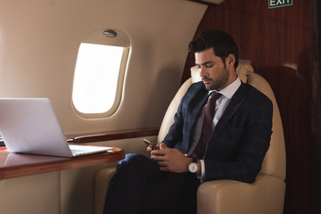 businessman working on smartphone and laptop in plane during business trip