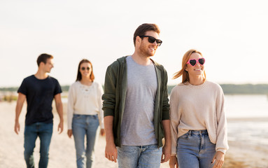 friendship, leisure and people concept - group of happy friends walking along beach in summer