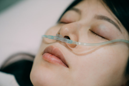 nasal cannula deliver oxygen for patient suffering respiratory disease. closed up view of sick asian woman face lying in bed in hospital room with tool to help her breath. Terminally ill female
